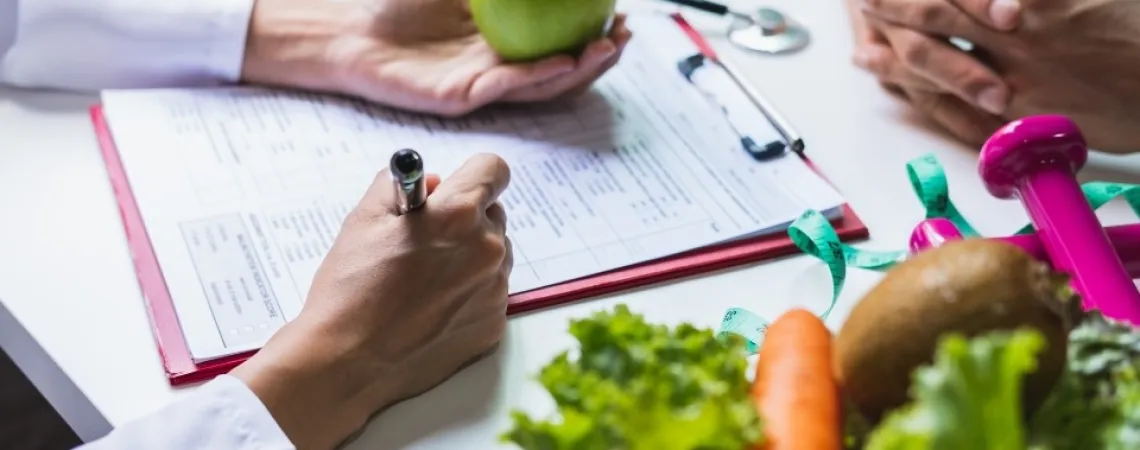 Nutritionniste-diététiste à Toronto qui fait une consultation en nutrition avec un client en tenant une pomme et en prenant des notes.