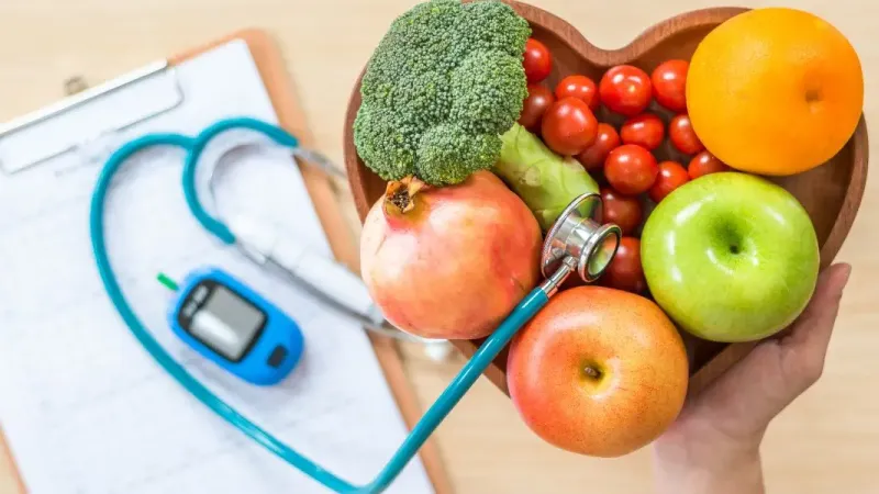 Triglycérides : des gestes concrets pour un taux plus sain. a person holding a stethoscope next to a bowl of fruits and vegetables