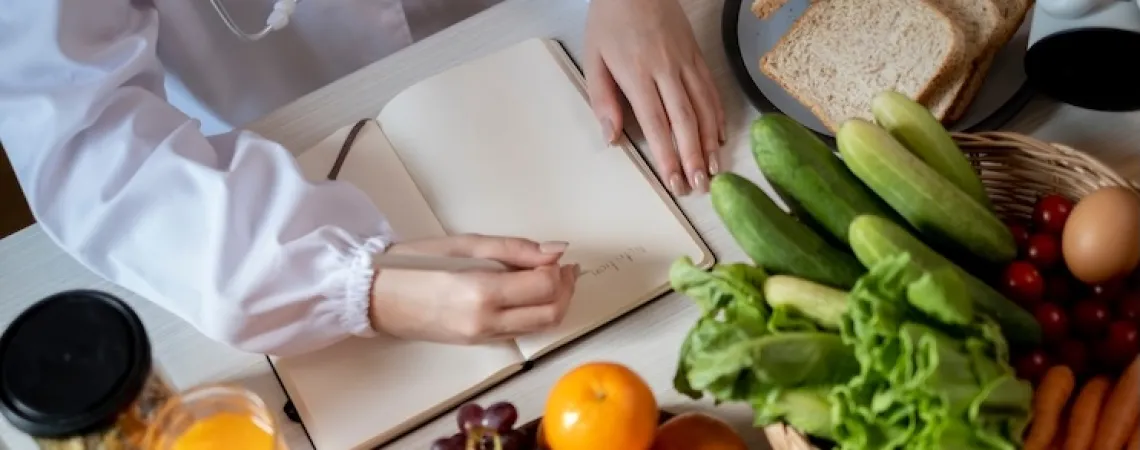 Une nutritionniste à Laval en blouse blanche écrit sur un bloc-notes entourée de fruits et légumes frais