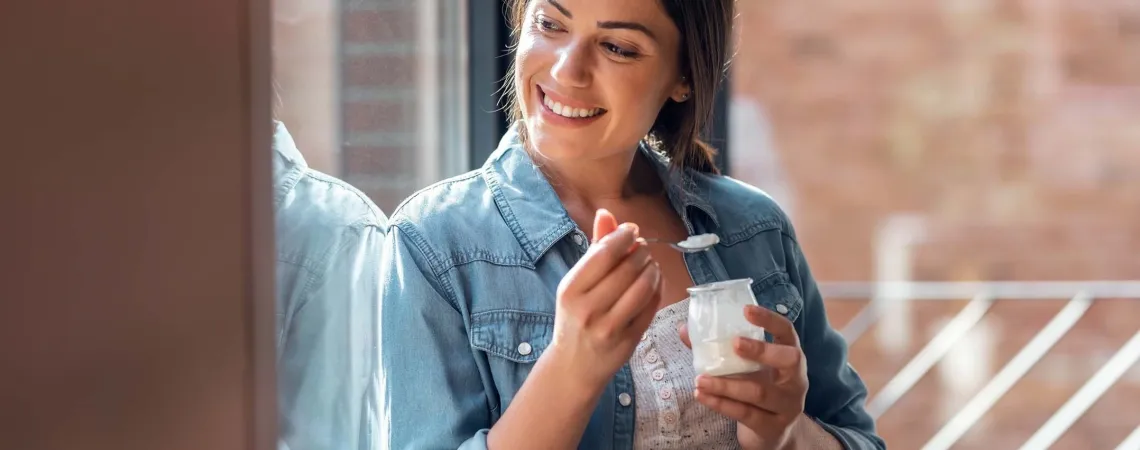 Une femme souriante mange du yaourt près d'une fenêtre - A smiling woman eating yogurt near a window