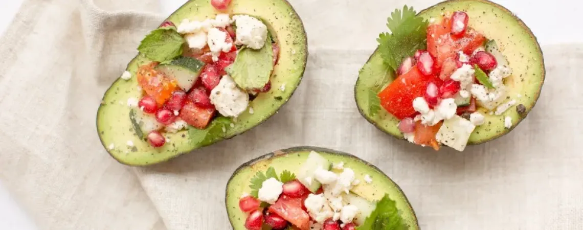 Trois moitiés d'avocat farcies avec feta, tomates, menthe et grenade