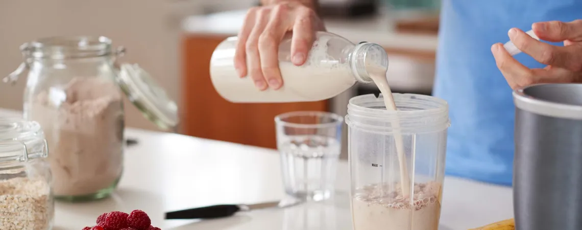 A person in a blue shirt pours a protein shake into a blender cup - Une personne en t-shirt bleu verse un shake de protéines dans un gobelet