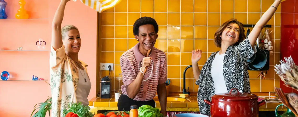Trois amis souriants s’amusent ensemble dans une cuisine colorée - Three smiling friends have fun together in a colorful kitchen