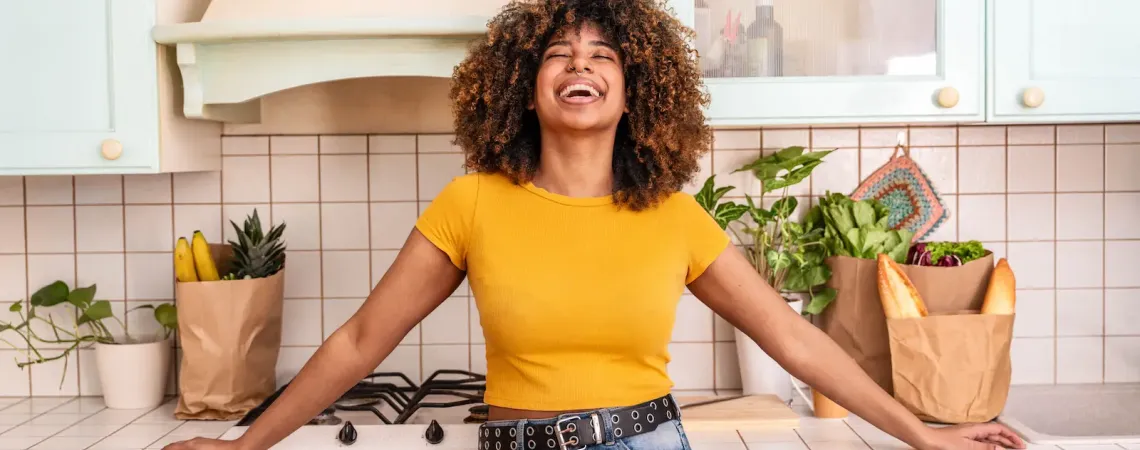 Femme souriante appuyée sur le comptoir de sa cuisine - Smiling woman leaning on her kitchen counter with grocery bags