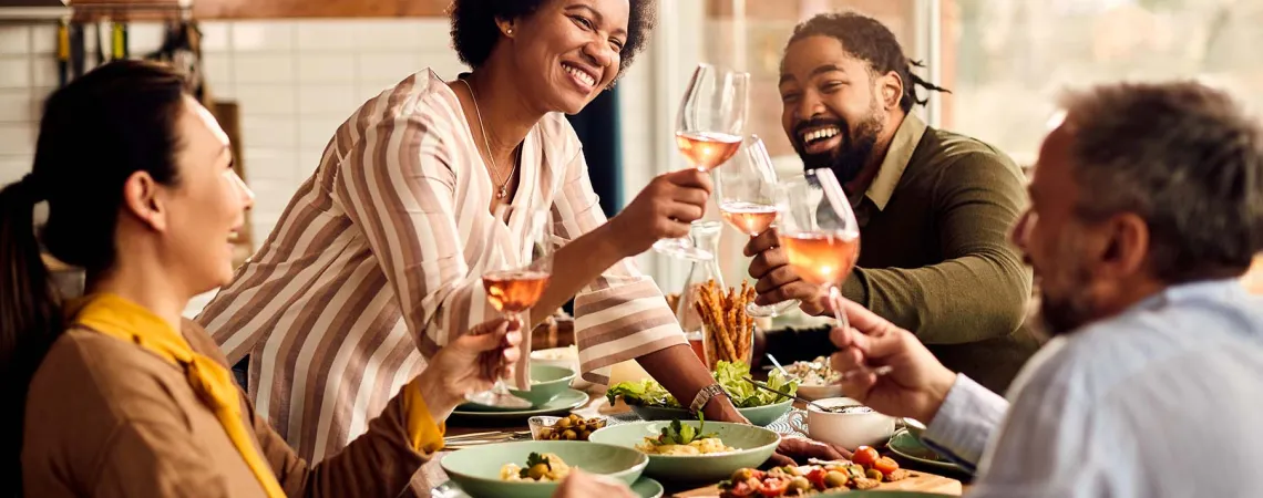 Groupe d'amis multiculturels trinquant avec des verres de vin rosé autour d'un repas - Multicultural group of friends toasting with glasses of rosé wine around a meal