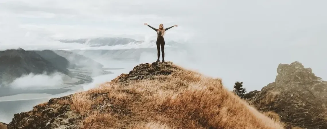 Une femme avec les bras en croix au sommet d'une montagne.