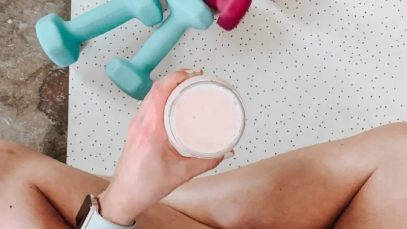 Haltères sur un tapis d'entrainement et main tenant un smoothie