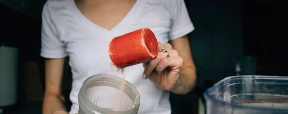 Femme qui met un tasse de protéines dans un malaxeur