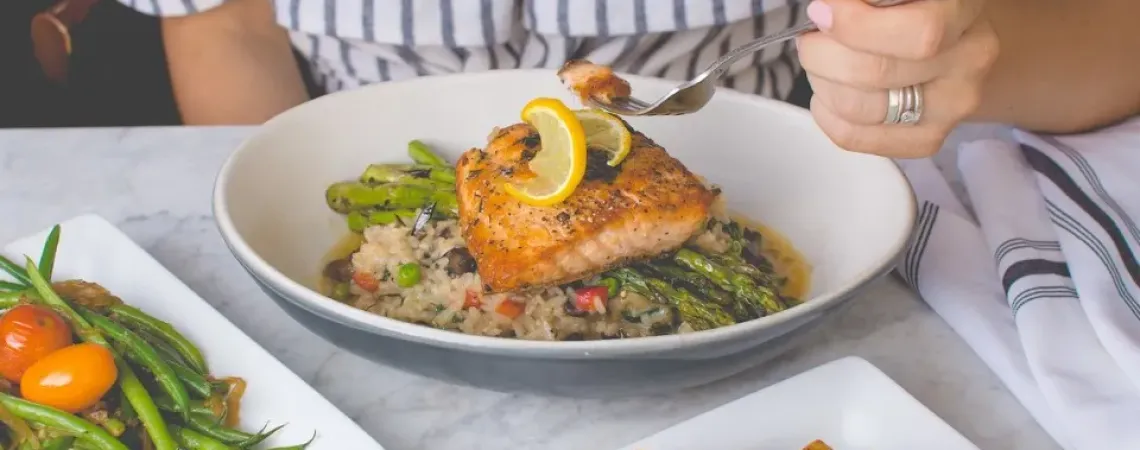 Femme qui mange du saumon sur lit d'asperges et riz aux légumes