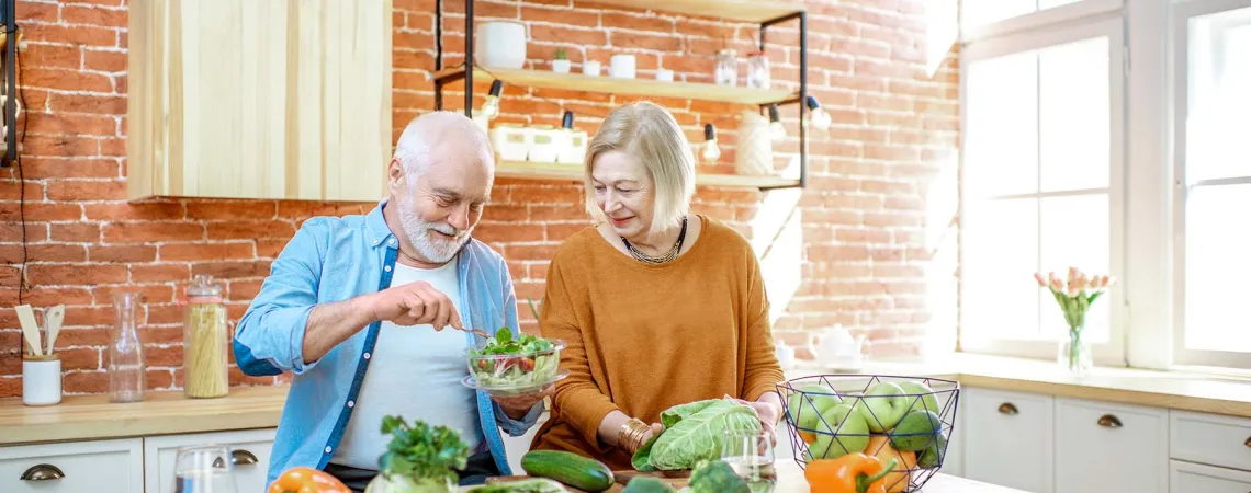 Deux jeunes femmes discutent lors d'une consultation en nutrition, assises à une table blanche dans une cuisine lumineuse. L'une d'elles explique avec des gestes, tandis que l'autre écoute attentivement.