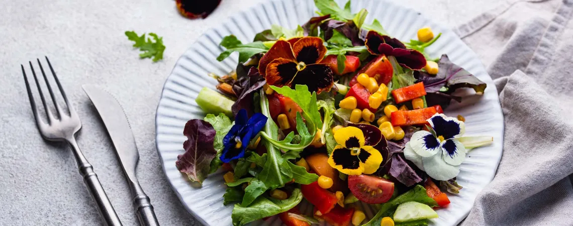 Une salade colorée garnie de fleurs comestibles, avec des légumes variés et des pensées violettes, jaunes et blanches - A colourful salad garnished with edible flowers, featuring various vegetables and purple, yellow, and white pansies