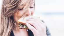 Fille qui mange un sandwich avec du vent dans les cheveux