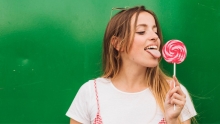Fille avec une chandail blanc qui lèche un suçon sur un fond vert