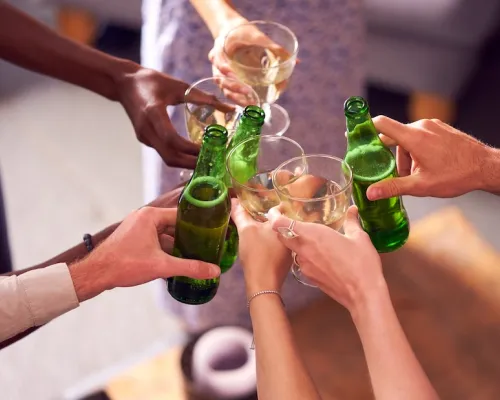 Un groupe de mains diverses trinquant avec des bouteilles de bière verte et des verres de vin dans une ambiance festive.
