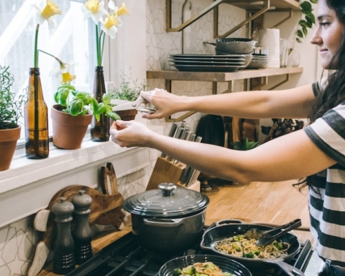 femme dans une cuisine cuisinant un plat et ajoutant du basilic