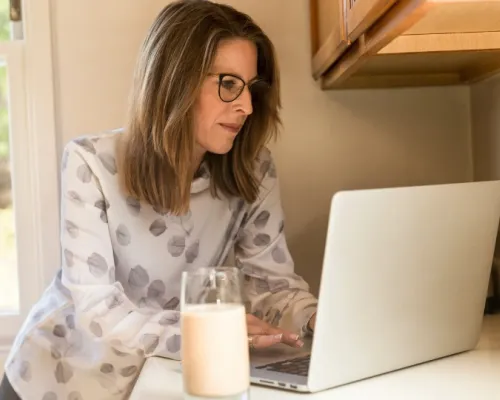 femme ménopausé devant un ordinateur avec un verre de lait