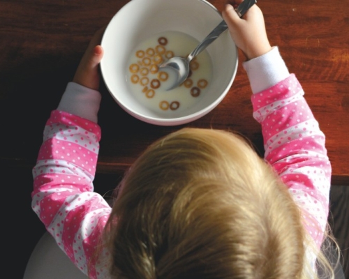 Enfant habillée en rose mangeant un bol de céréales avec du lait