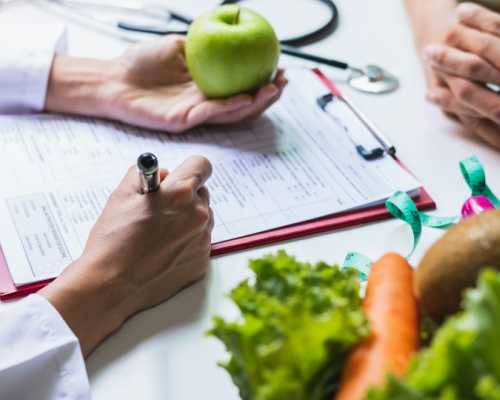 Nutritionniste-diététiste à Toronto qui fait une consultation en nutrition avec un client en tenant une pomme et en prenant des notes.