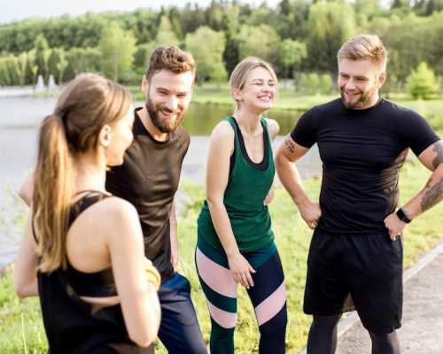 Un groupe de quatre amis en tenue de sport souriant et discutant à l'extérieur près d'un lac, avec une zone boisée en arrière-plan.