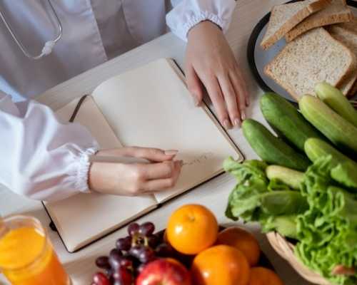 Une nutritionniste à Laval en blouse blanche écrit sur un bloc-notes entourée de fruits et légumes frais