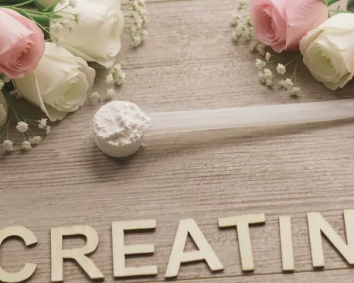 Cream and pink roses with small white blossoms arranged on a light wooden background next to a wooden spoon-shaped scoop and the word “CREATINE” in gold letters.
