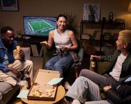 Quatre amis rient et mangent de la pizza dans un salon confortable en regardant un match de football américain à la télévision