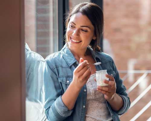 Une femme souriante mange du yaourt près d'une fenêtre - A smiling woman eating yogurt near a window