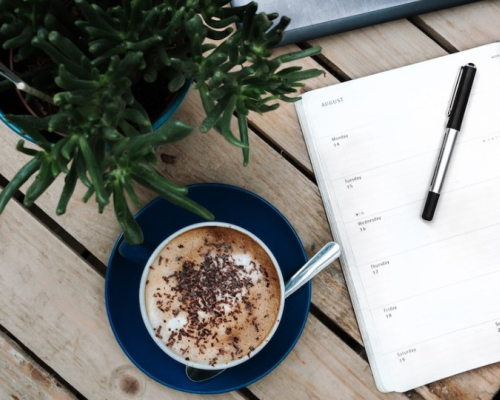 Un agenda, un café et une plante sur une table en bois