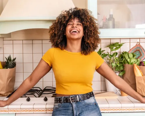 Femme souriante appuyée sur le comptoir de sa cuisine - Smiling woman leaning on her kitchen counter with grocery bags