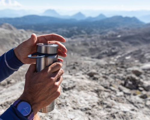 Mains ouvrant une bouteille d'eau en montagne.