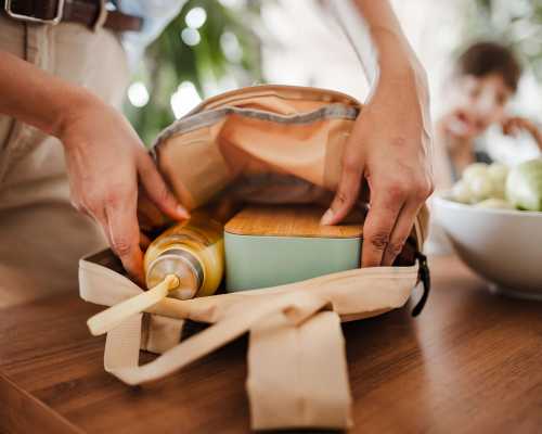 Personne en train de préparer un sac avec une boîte à lunch et une bouteille - Person packing a bag with a lunchbox and a bottle