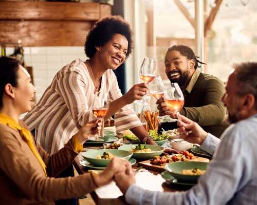 Groupe d'amis multiculturels trinquant avec des verres de vin rosé autour d'un repas - Multicultural group of friends toasting with glasses of rosé wine around a meal