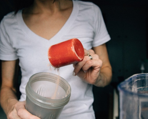 Femme qui met un tasse de protéines dans un malaxeur