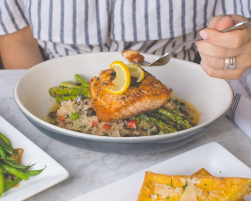 Femme qui mange du saumon sur lit d'asperges et riz aux légumes