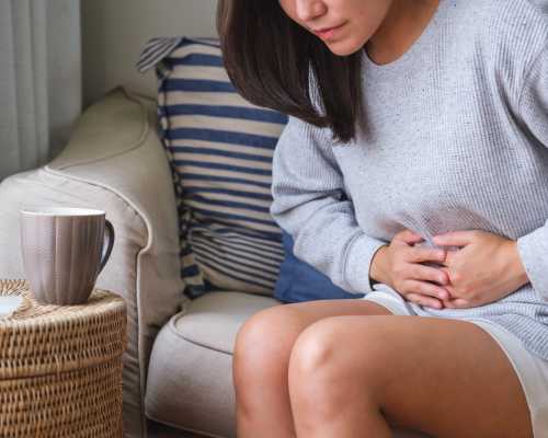 Femme souffrant de maux d'estomac et de douleurs abdominales assise sur un canapé à la maison
