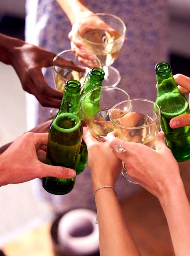 Un groupe de mains diverses trinquant avec des bouteilles de bière verte et des verres de vin dans une ambiance festive.