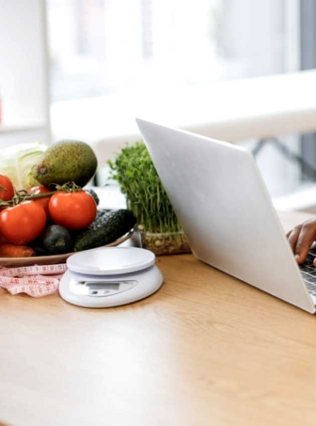 Un nutritionniste diététiste en blouse blanche travaille sur un ordinateur portable avec des fruits, légumes et suppléments sur la table.