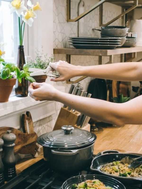 femme dans une cuisine cuisinant un plat et ajoutant du basilic