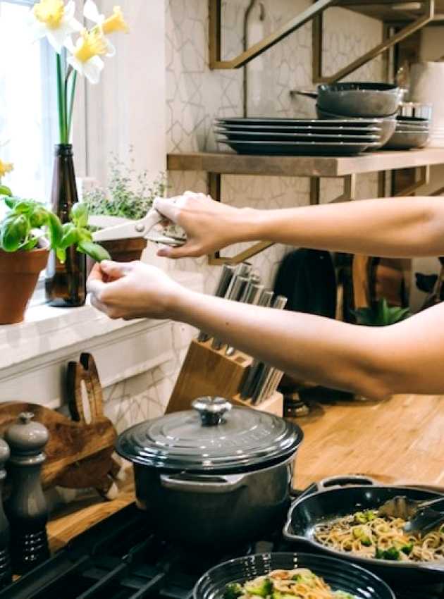 femme dans une cuisine cuisinant un plat et ajoutant du basilic