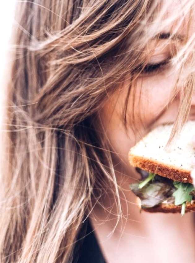 Fille qui mange un sandwich avec du vent dans les cheveux