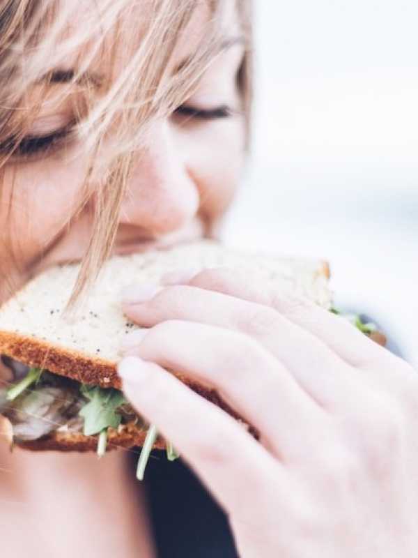 Fille qui mange un sandwich avec du vent dans les cheveux