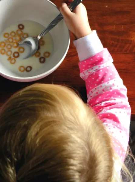 Enfant habillée en rose mangeant un bol de céréales avec du lait