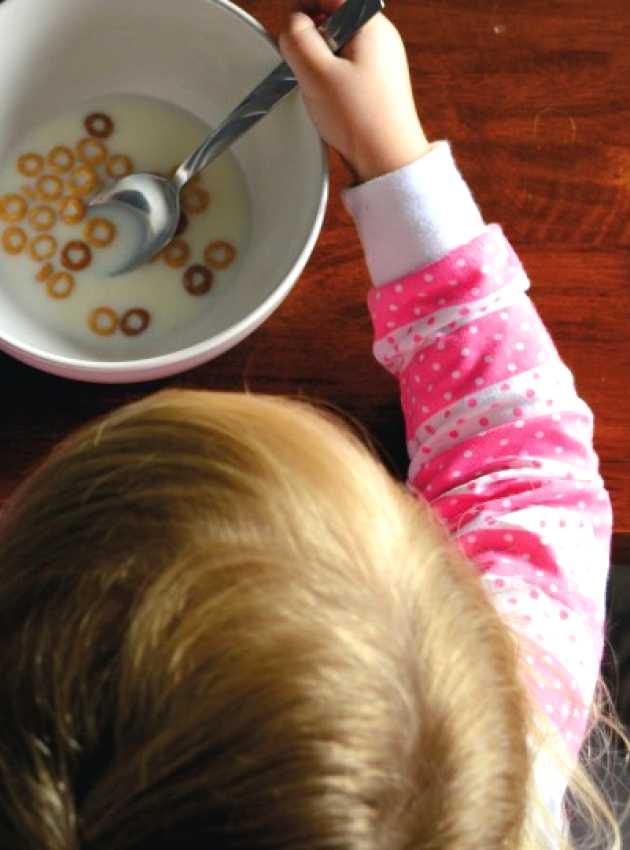 Enfant habillée en rose mangeant un bol de céréales avec du lait