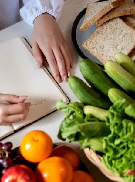 Une nutritionniste à Laval en blouse blanche écrit sur un bloc-notes entourée de fruits et légumes frais
