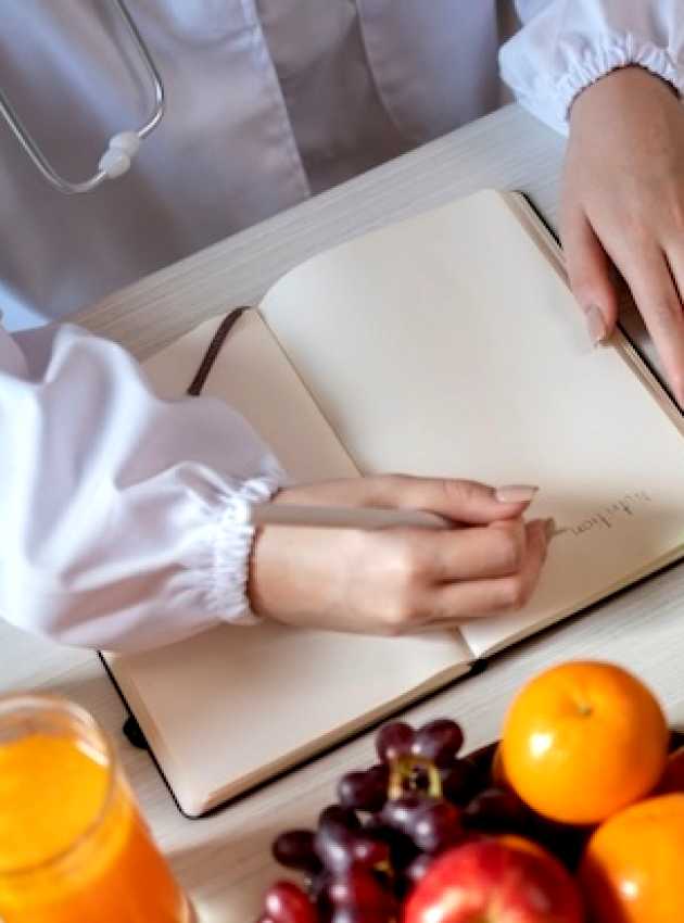 Une nutritionniste à Laval en blouse blanche écrit sur un bloc-notes entourée de fruits et légumes frais