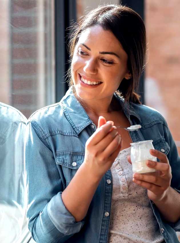 Une femme souriante mange du yaourt près d'une fenêtre - A smiling woman eating yogurt near a window