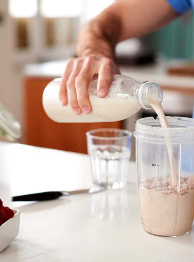 A person in a blue shirt pours a protein shake into a blender cup - Une personne en t-shirt bleu verse un shake de protéines dans un gobelet