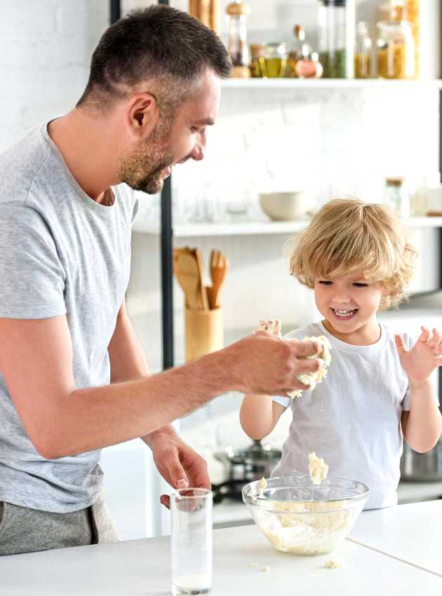 Un père et son fils rient et s'amusent en préparant de la pâte dans une cuisine moderne et lumineuse - A father and his son are laughing and having fun while making dough in a bright, modern kitchen