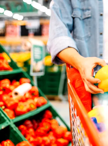 A shopper selects a yellow pepper from a display of fresh produce at the grocery store.