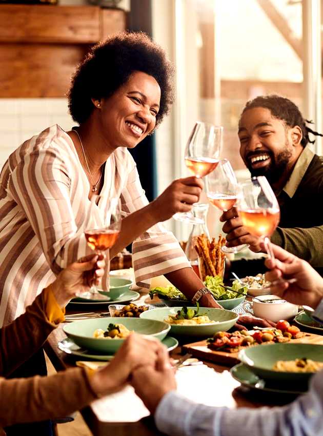 Groupe d'amis multiculturels trinquant avec des verres de vin rosé autour d'un repas - Multicultural group of friends toasting with glasses of rosé wine around a meal